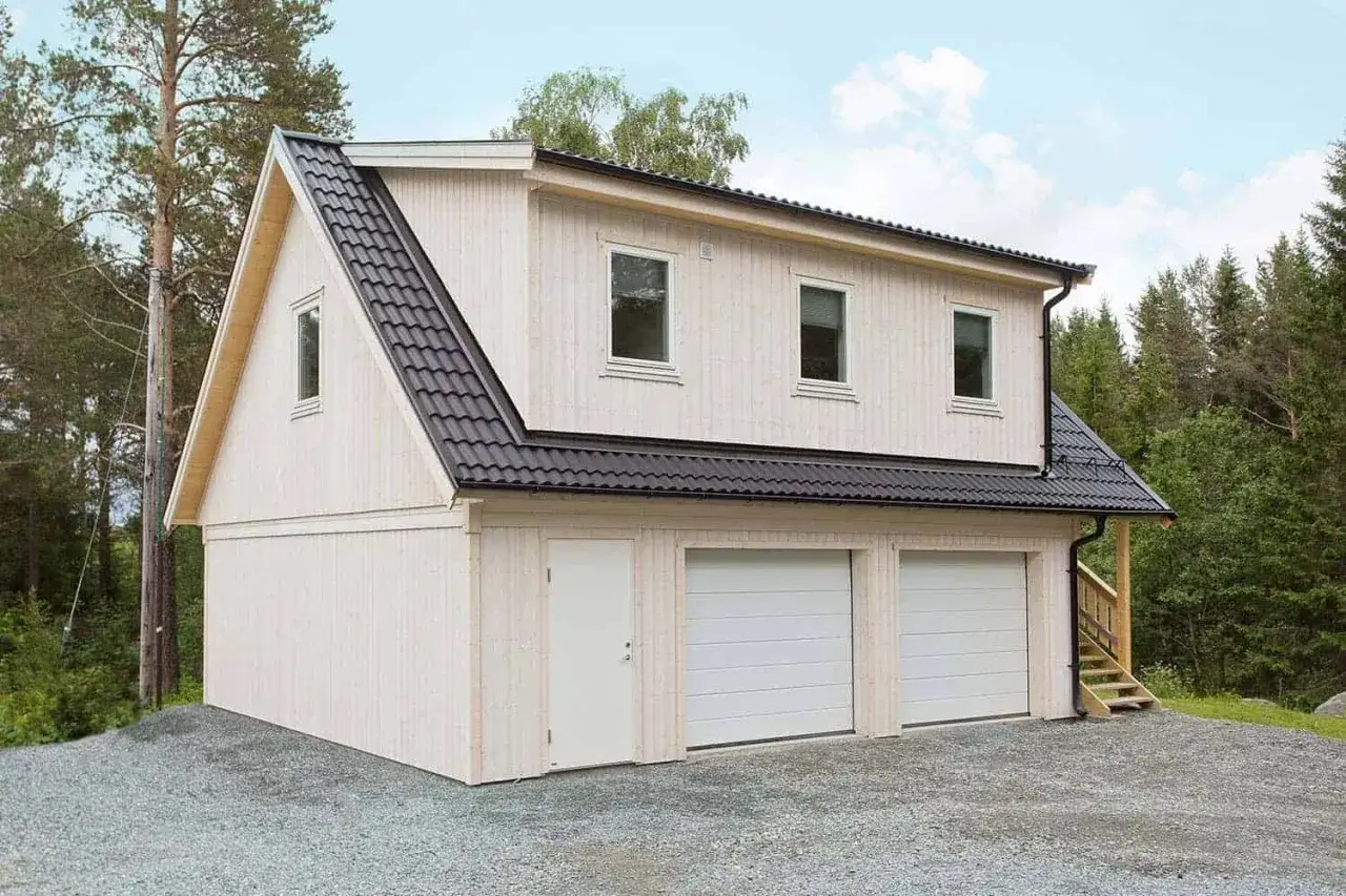 Ett modernt garage med två portar och en dörr, redo att bygga om till bostad. Omgiven av skog.