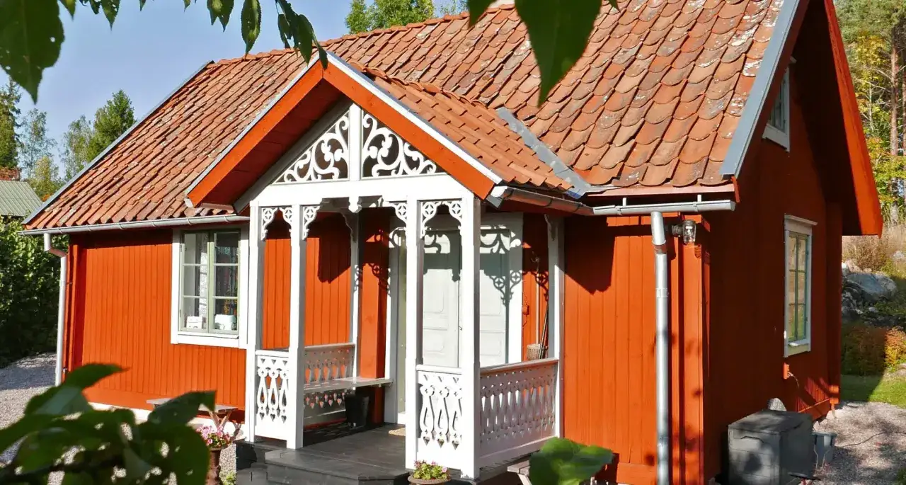Ett vackert r&ouml;tt hus med tegeltak och en vit, snickarglad farstukvist. Perfekt f&ouml;r att bygga farstukvist och skapa en inbjudande entr&eacute;.