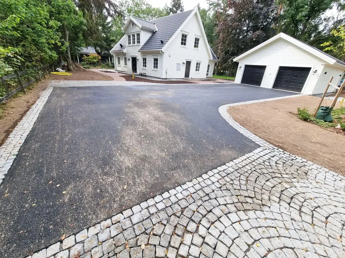 Nyasfalterad uppfart med vackra stenkanter framför ett vitt hus och garage.