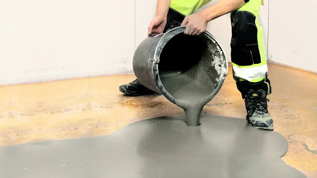 En person häller ut flytande betong ur en hink för att bila golv.