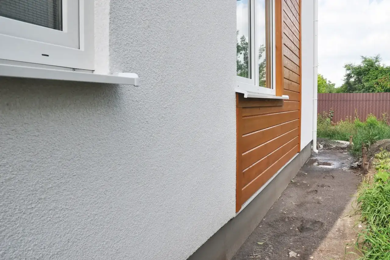 Nyrenoverad fasad med vit puts och träpanel. Ett fönster med vit karm syns.