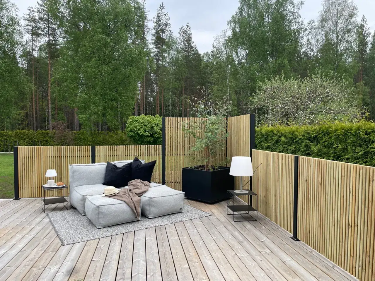 Modern trädgårdsdesign med en stilren träpanel som ger staket inspiration. En bekväm loungegrupp och lampor skapar en inbjudande uteplats.