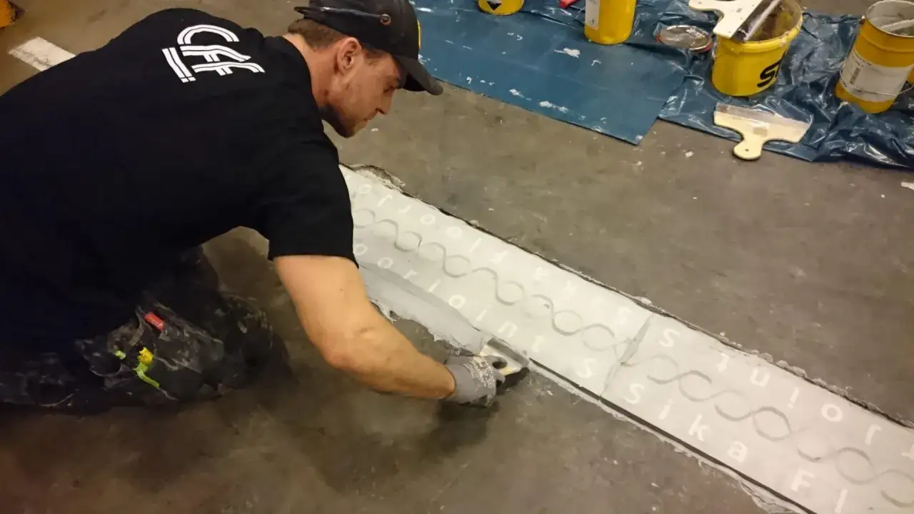 Man lagar betonggolv med spackel och fogmassa.