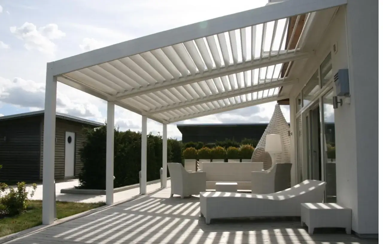 Modern vit pergola med justerbara lameller. Perfekt för att skapa en skuggig uteplats, kanske med tanke på pergola bygglov. Utemöbler i vitt.