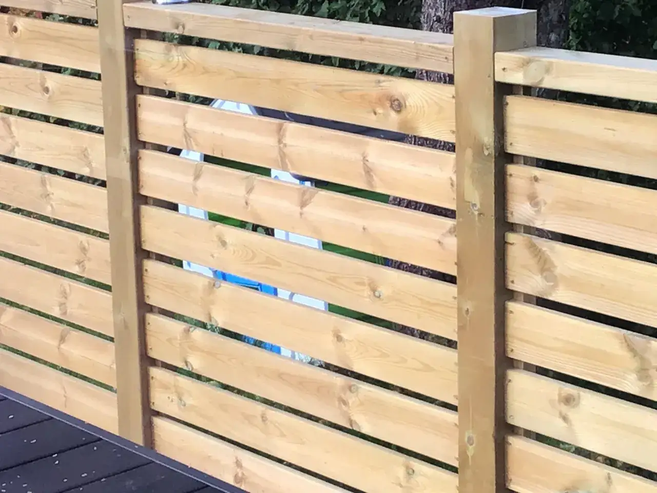 Staket med liggande ribbor av olika bredd, monterade på trästolpar.