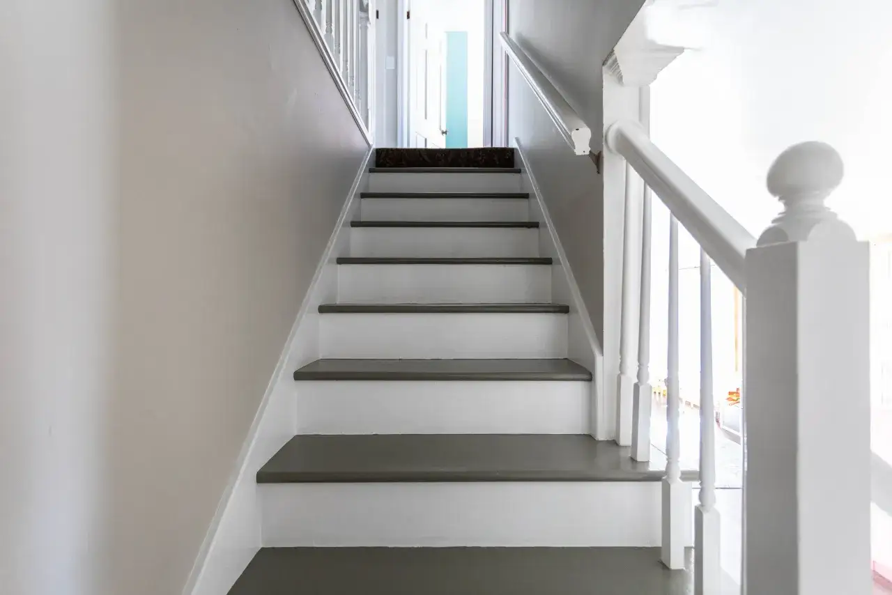 En vitm&aring;lad trappa med m&ouml;rkgr&aring; steg, redo f&ouml;r renovering. En ny matta p&aring; &ouml;versta steget ger en k&auml;nsla av p&aring;g&aring;ende projekt.