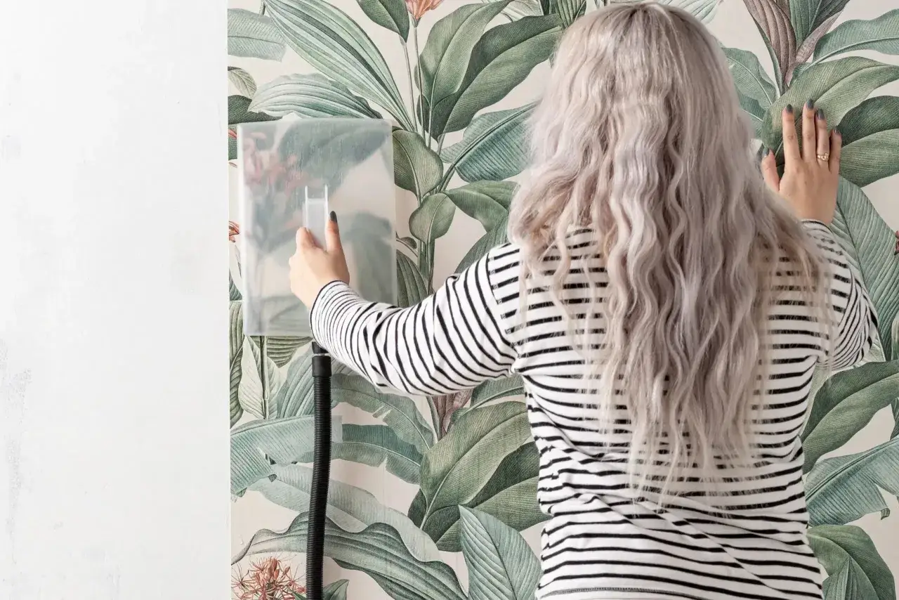 Kvinna med blont hår använder en ångmaskin för att riva tapet med blommönster.