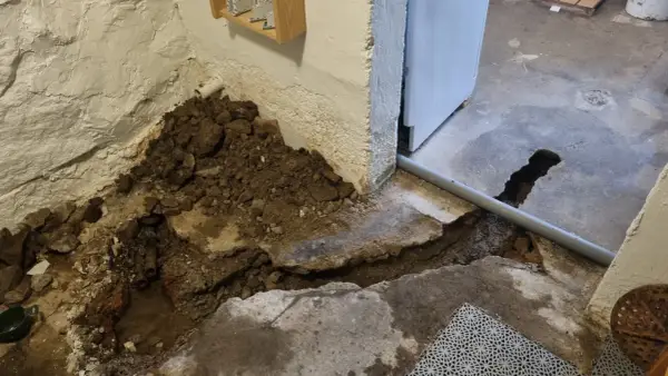 Hål i betonggolvet visar på pågående arbete med att laga rör. Jord och sten ligger uppgrävt vid väggen.