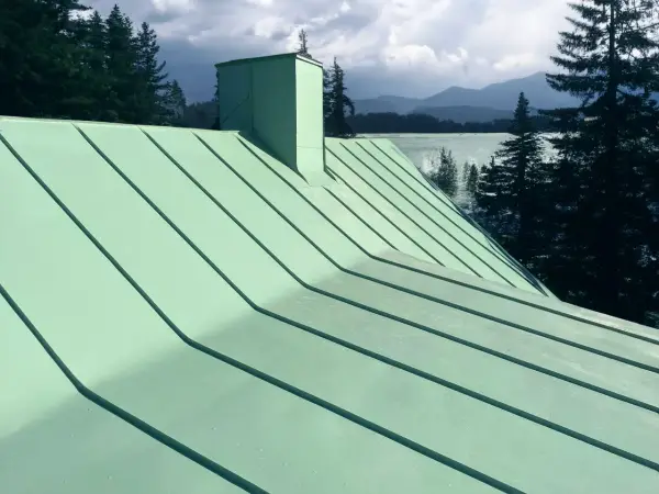 Grönt plåttak med skorsten, vacker utsikt över sjö och berg. Tänk på kostnad plåttak vid renovering.